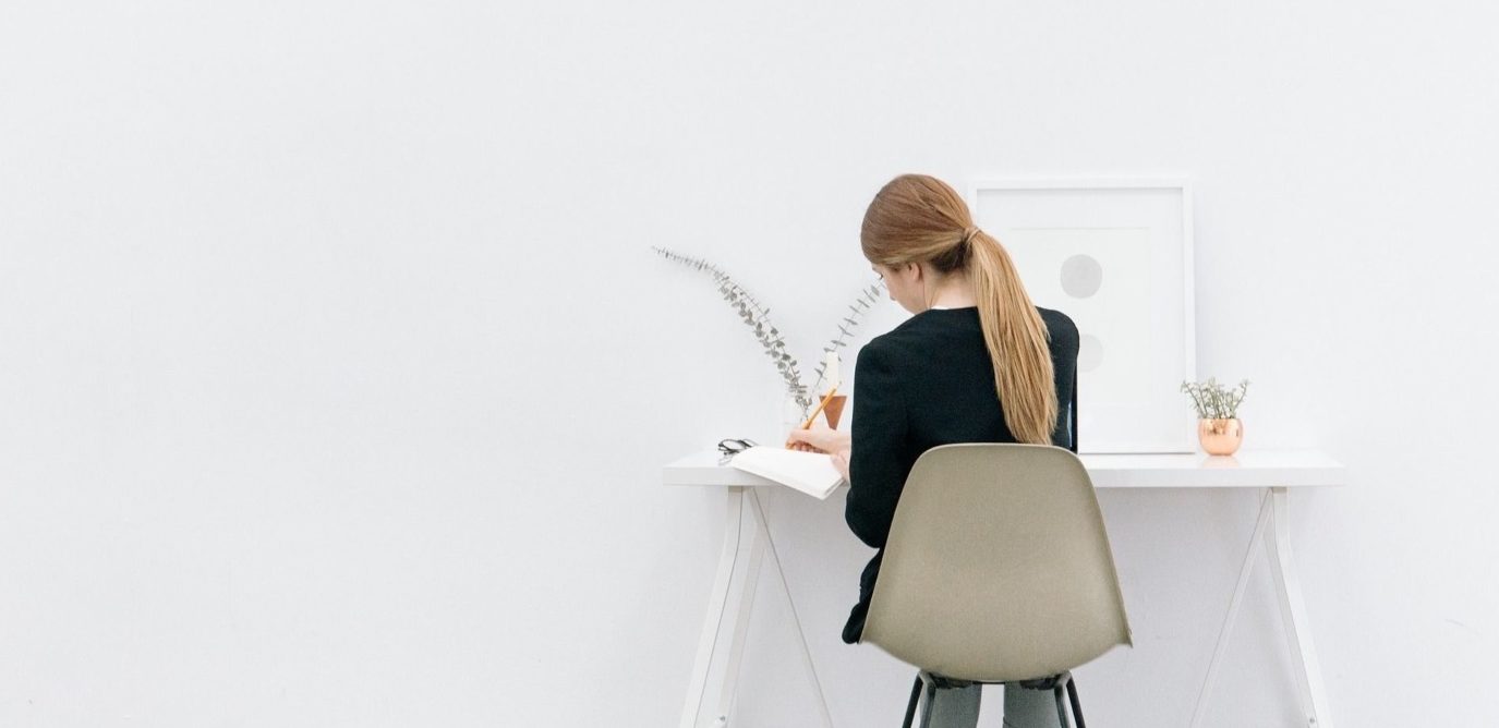 Woman sat writing on white desk