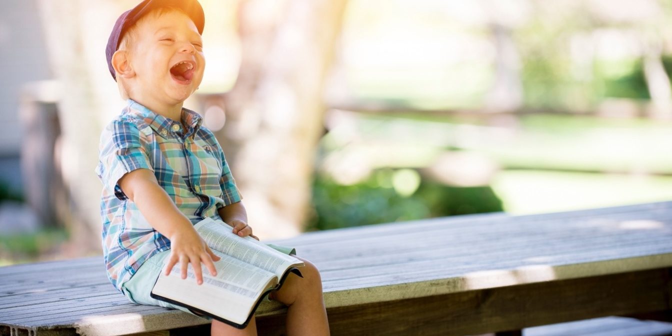 Young boy laughing whilst holding a book