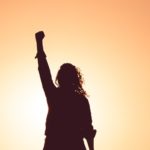 Woman raising fist against sunset - courage