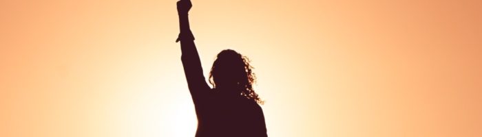 Woman raising fist against sunset - courage