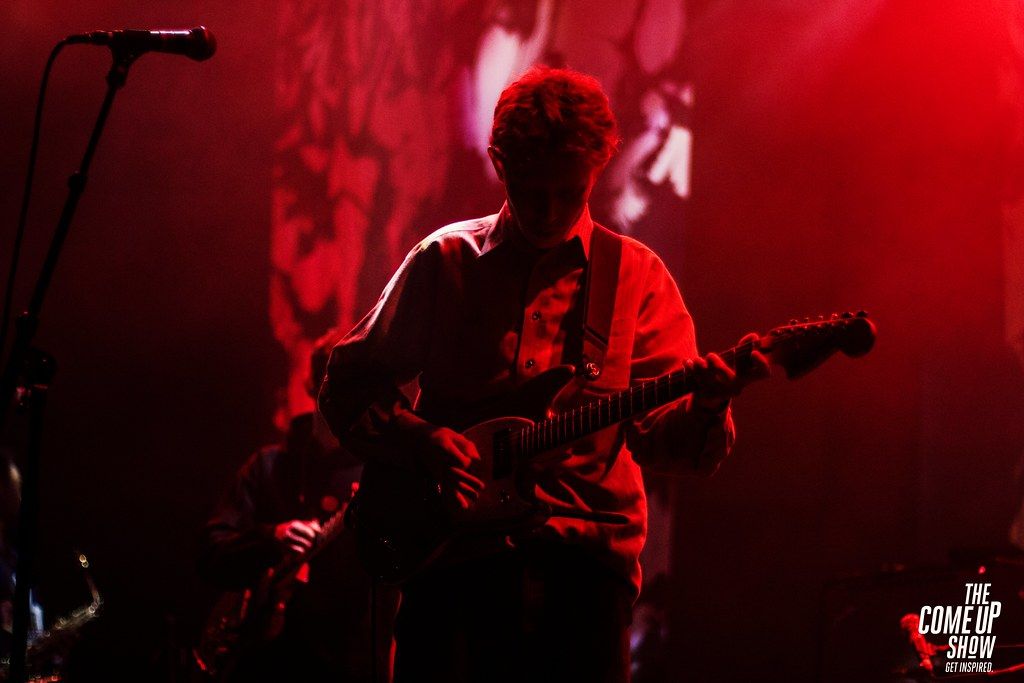 king krule on stage, red background, with a guitar