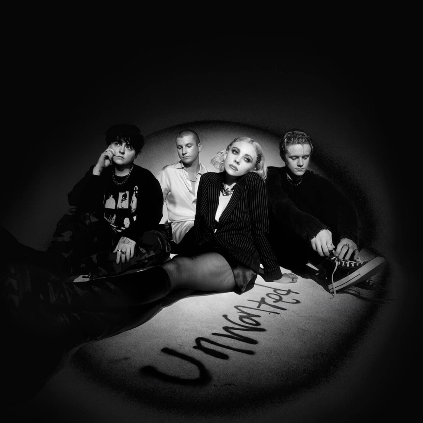 The cover of Unwanted, it features the band sat in a dark room with a spotlight shining on them and the word Unwanted spray painted on the floor