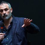 An image of the director Alex Garland holding a mic and speaking to an unseen audience.