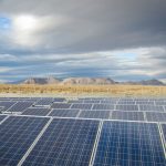 A solar farm in the foreground, with mountains and a desert in the background.