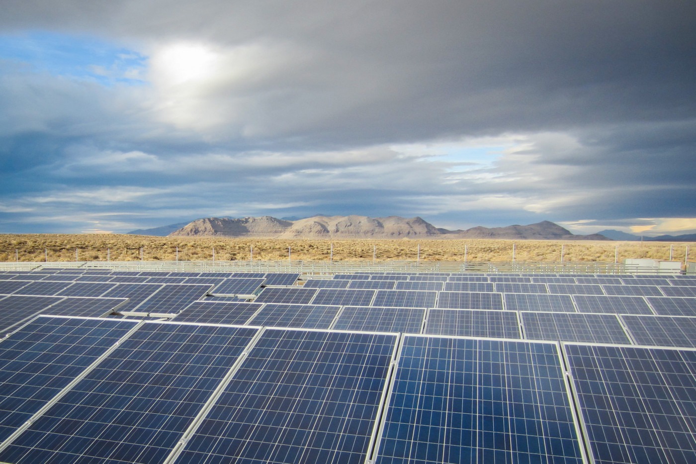 A solar farm in the foreground, with mountains and a desert in the background.