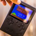 Black gameboy with retro Super Mario startscreen with a light brown blurry background.