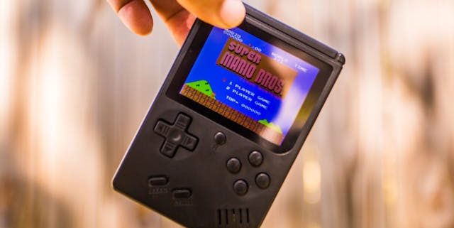 Black gameboy with retro Super Mario startscreen with a light brown blurry background.