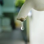 A drop of water dripping from a white tap. Header image.