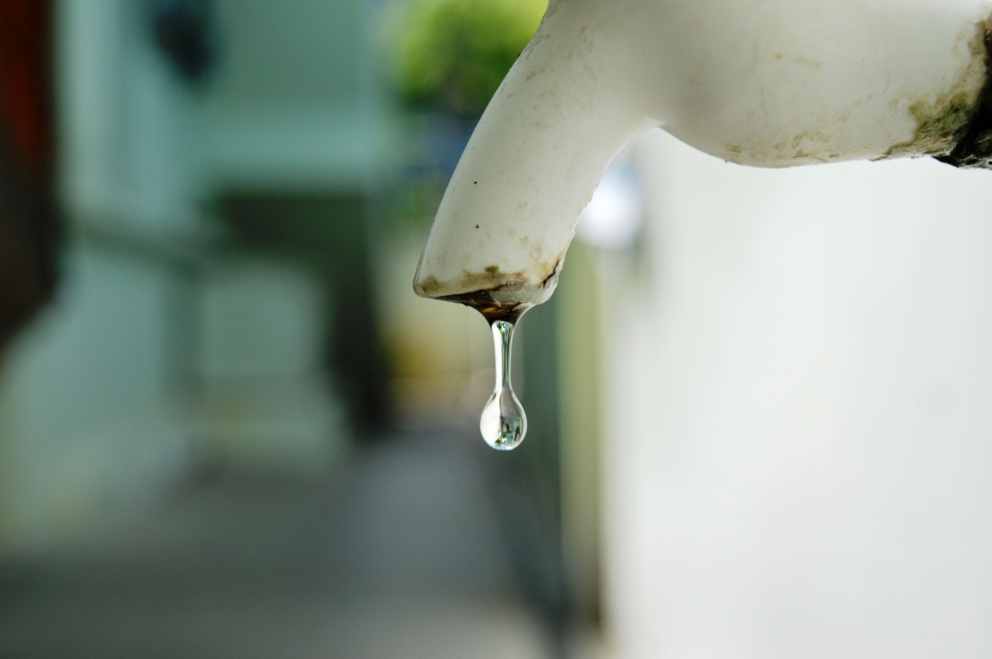 A drop of water dripping from a white tap. Header image.