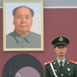 Chinese soldier guarding the southern entrance of the Forbbiden City in Beijing, dominated by a giant portrait of Mao Zedong.