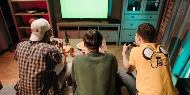 Three boys playing video games facing their backs towards us