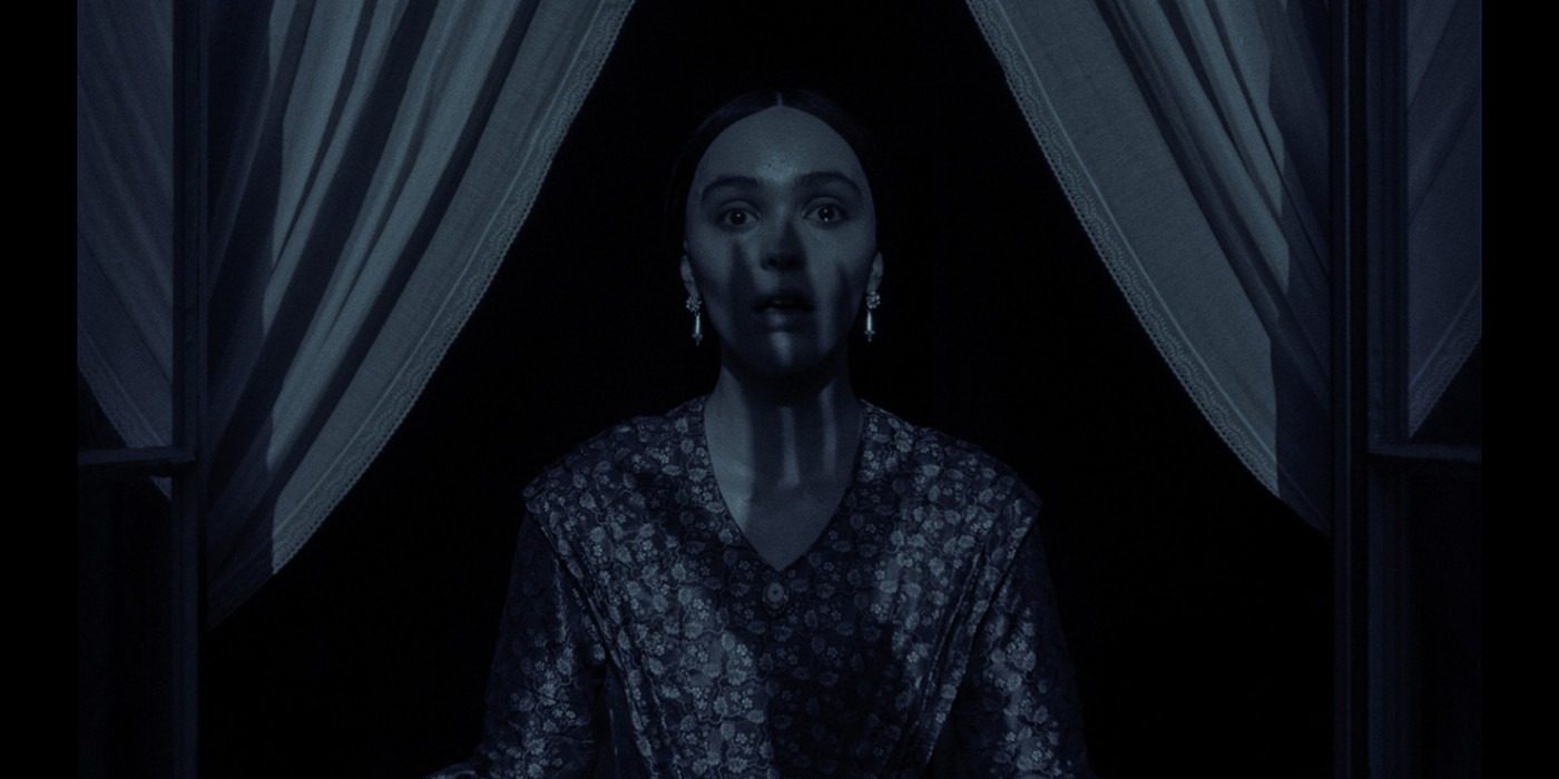 A woman looks afraid as she looks out of her window at night, framed by curtains, as a strange and monstrous shadow of a hand covers her body and face