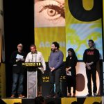 The filmmaker Emad Burnat stands at a podium with others at a film festival giving a speech