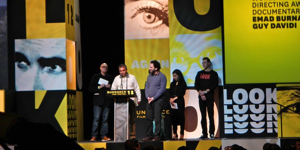 The filmmaker Emad Burnat stands at a podium with others at a film festival giving a speech