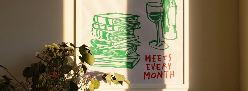A poster on a white wall that says "Meets Every Month" and has an illustration of books and wine on it
