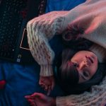 Teenage Girl Lying on Bed next to gaming laptop and controller