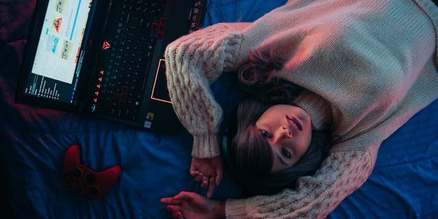 Teenage Girl Lying on Bed next to gaming laptop and controller