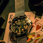 Playing cards, sunglasses, a silver watch, pistol and bullets laid out of a table