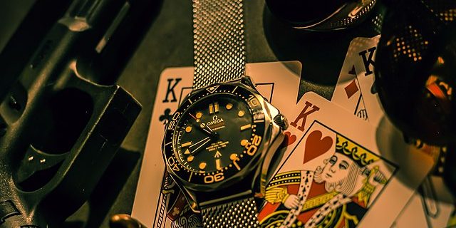 Playing cards, sunglasses, a silver watch, pistol and bullets laid out of a table