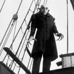 A still of the vampire Nosferatu from the 1922 silent film looking ominous aboard a boat