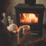 Image of woman sitting with a hot drink in front of a fireplace