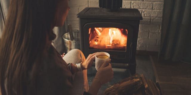 Image of woman sitting with a hot drink in front of a fireplace