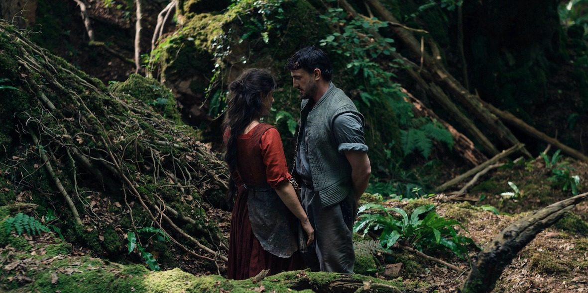 A man and a woman from the 16th century stand in the middle of an English forest looking into each others eyes