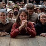 Jessie Buckley in Hamnet, stood in front of a stage