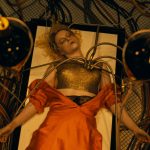 Still from "The Bride!" - A woman lies asleep on a hospital bed, tubes coming out of her shoulder