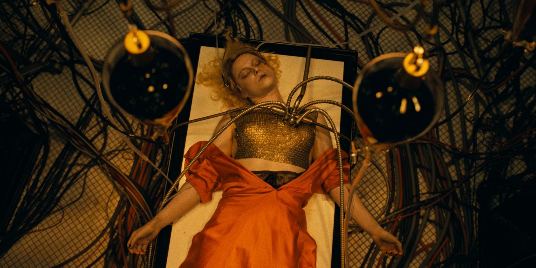 Still from "The Bride!" - A woman lies asleep on a hospital bed, tubes coming out of her shoulder