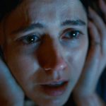 A close-up of a frightened woman gripping her headphones