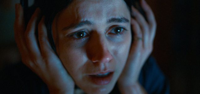 A close-up of a frightened woman gripping her headphones