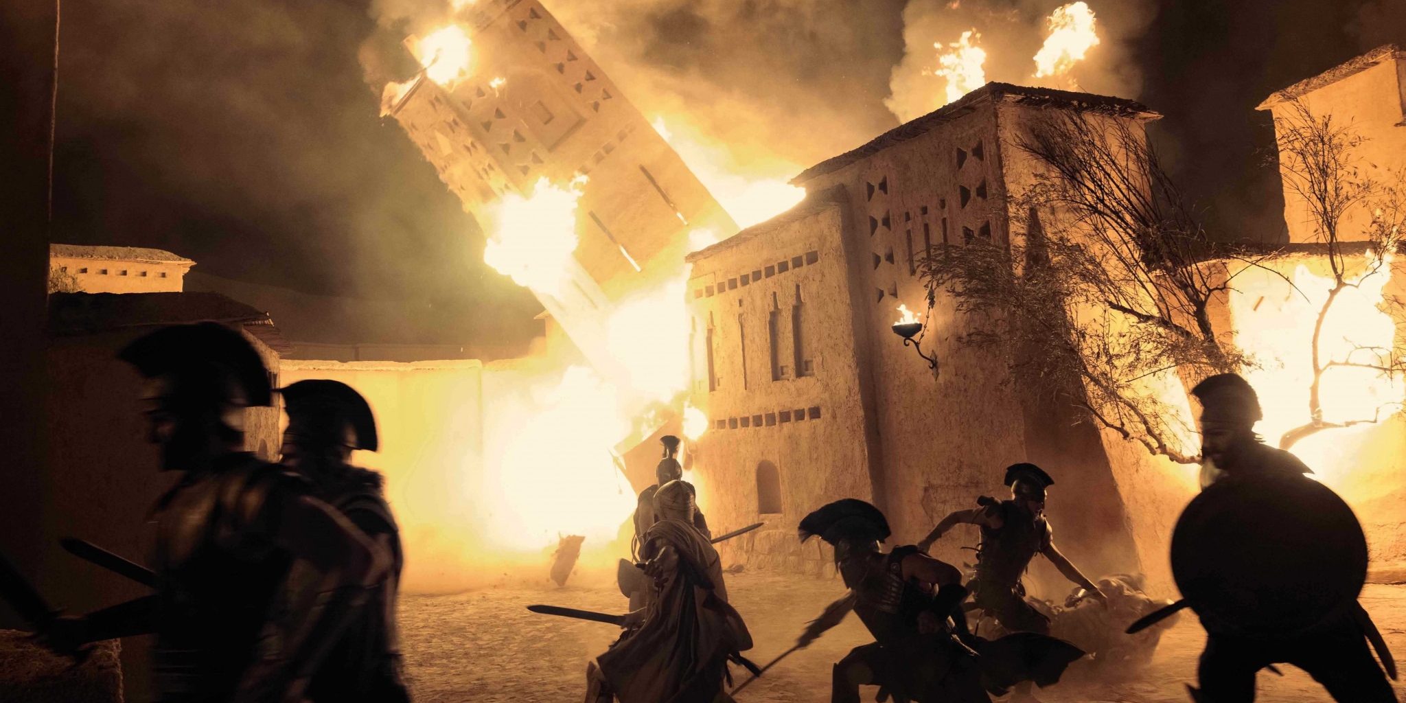 Ancient greek soldiers in a scene of the fall of Troy fight within the city as a burning building falls behind them