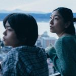Two people look over a balcony in a city