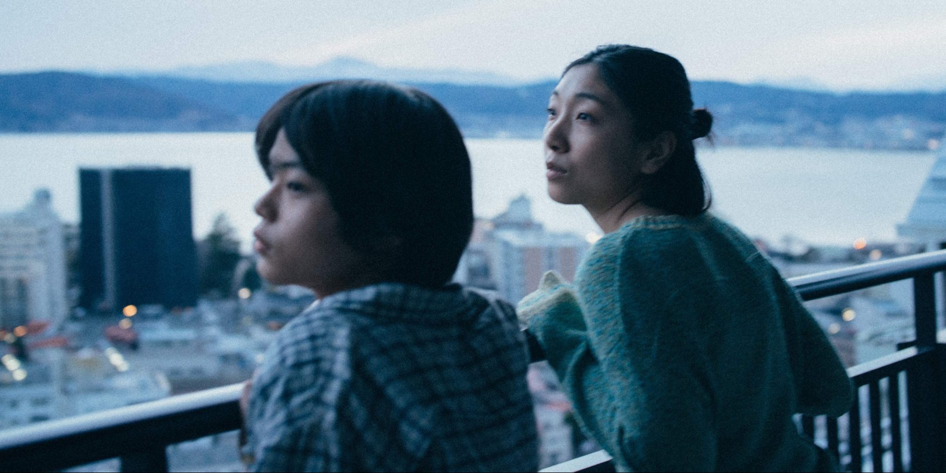 Two people look over a balcony in a city